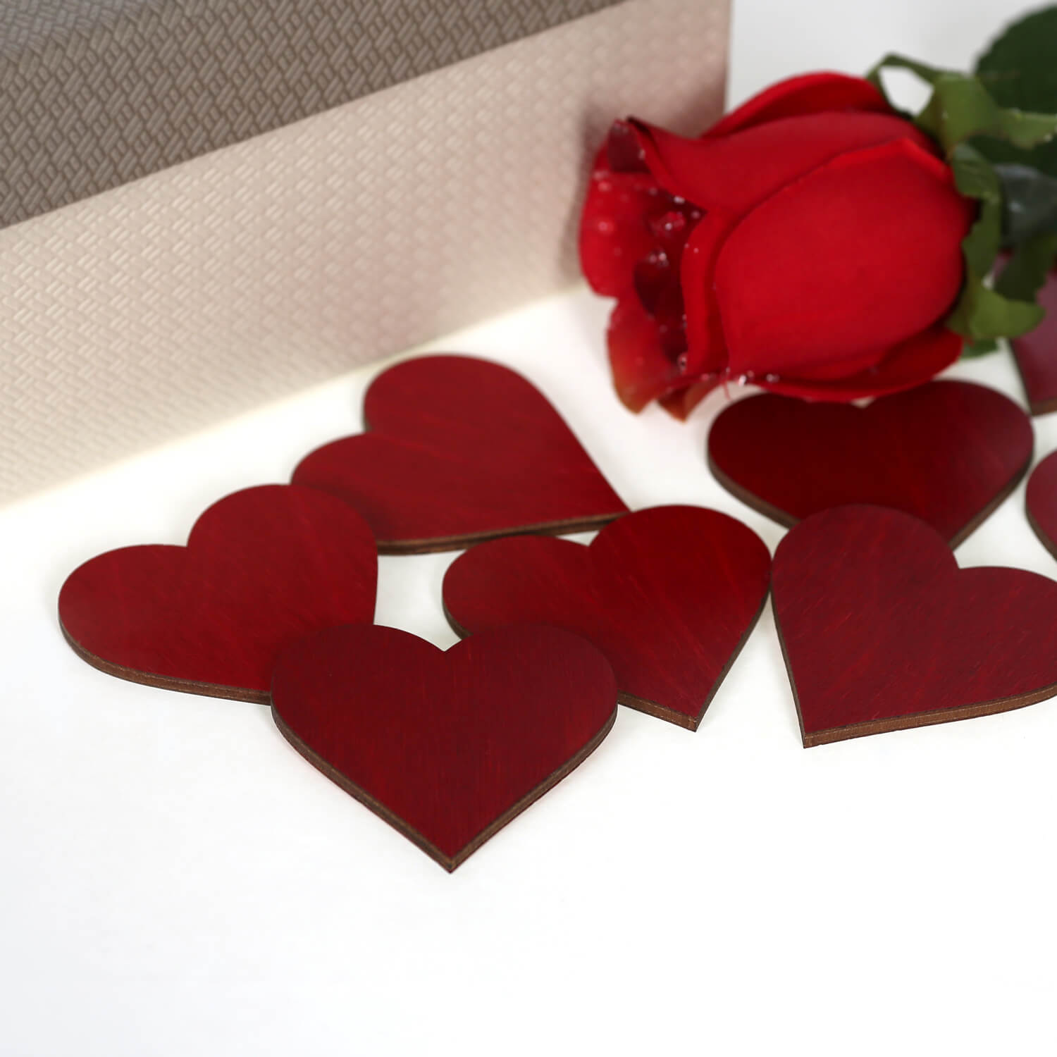 Gruppe dunkelroter Holzherzen mit roter Rose und Geschenkbox