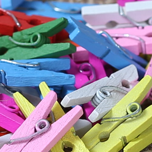 Viele bunte Mini-Holzwäscheklammern in Gelb, Pink, Blau, Grün und Grau mit Metallfeder, lose aufgeschüttet