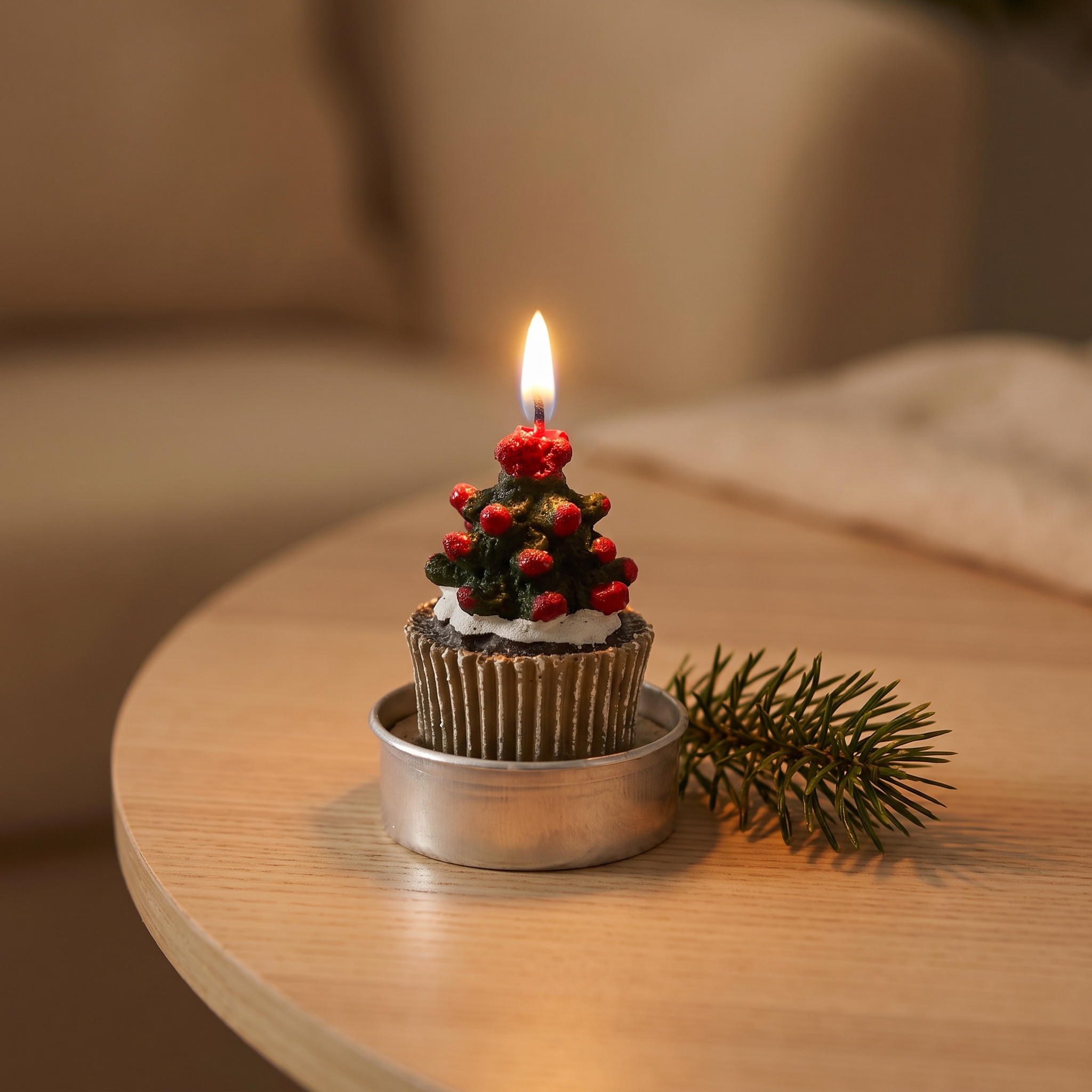 Brennendes Teelicht in Cupcake-Form mit grünem Weihnachtsbaum-Motiv und roten Beeren, in silberner Teelichthalterung auf Holztisch, daneben ein Tannenzweig